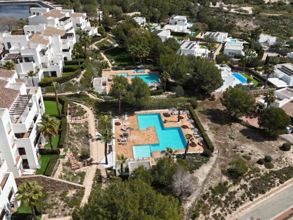 Aerial view of white villa-style buildings surrounding multiple blue swimming pools with terraces and palm trees.