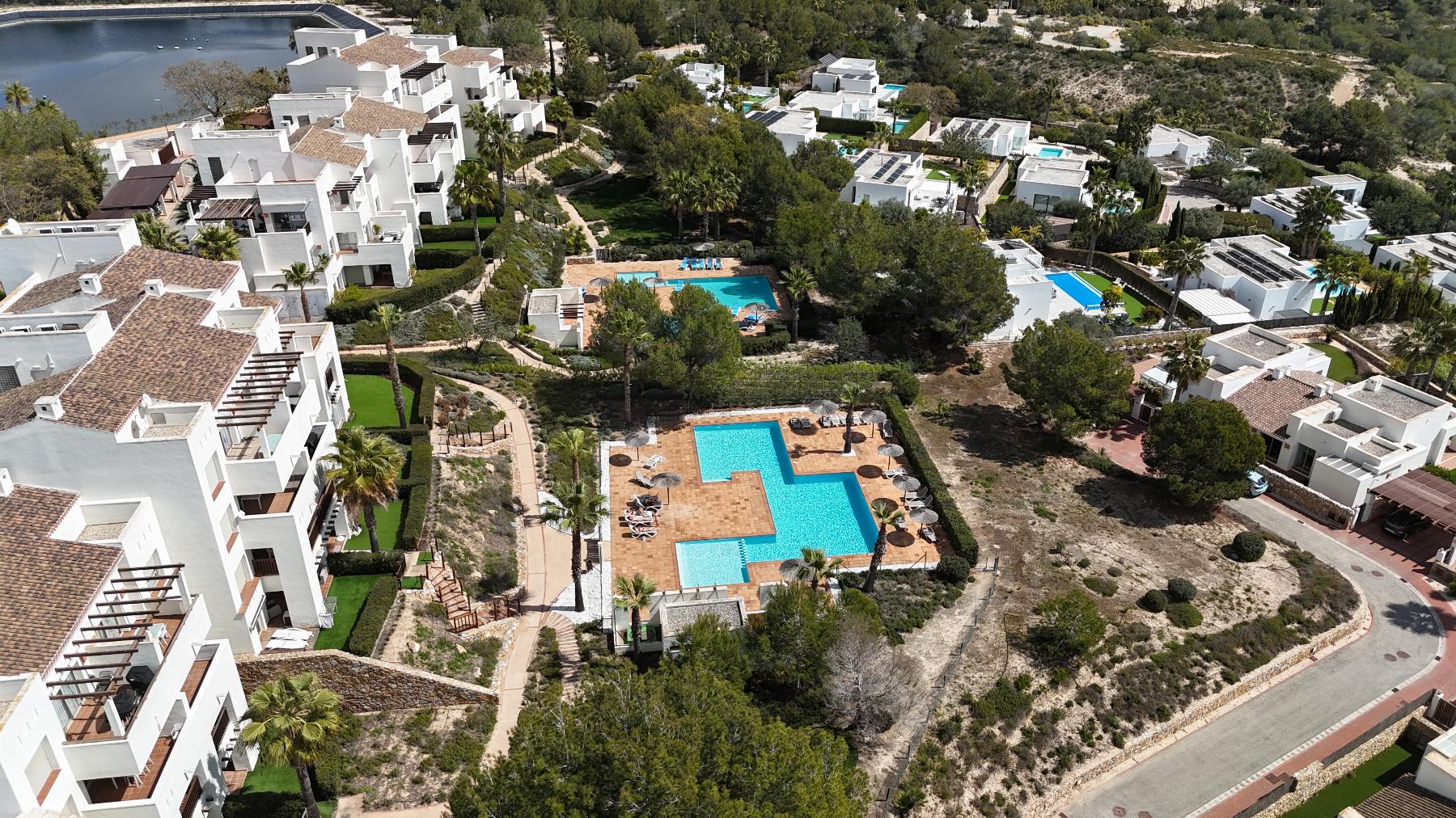 Aerial view of white villa-style buildings surrounding multiple blue swimming pools with terraces and palm trees.