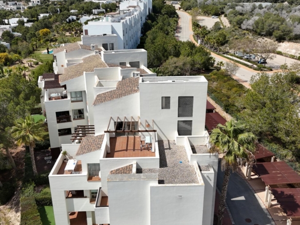 Aerial view of a white modern apartment complex with terracotta-tiled rooftops set among trees and a curving road nearby.