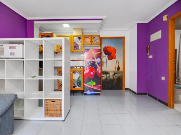 Bright interior with purple accent walls, white open shelving, and a back kitchen with orange cabinets and a floral-fruit refrigerator panel.