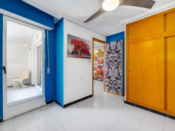 Interior hallway with blue walls, white trim, and a large wooden closet on the right. A framed red-tree artwork hangs on the wall; a patterned screen and a doorway lead to another room with colorful decor visible.