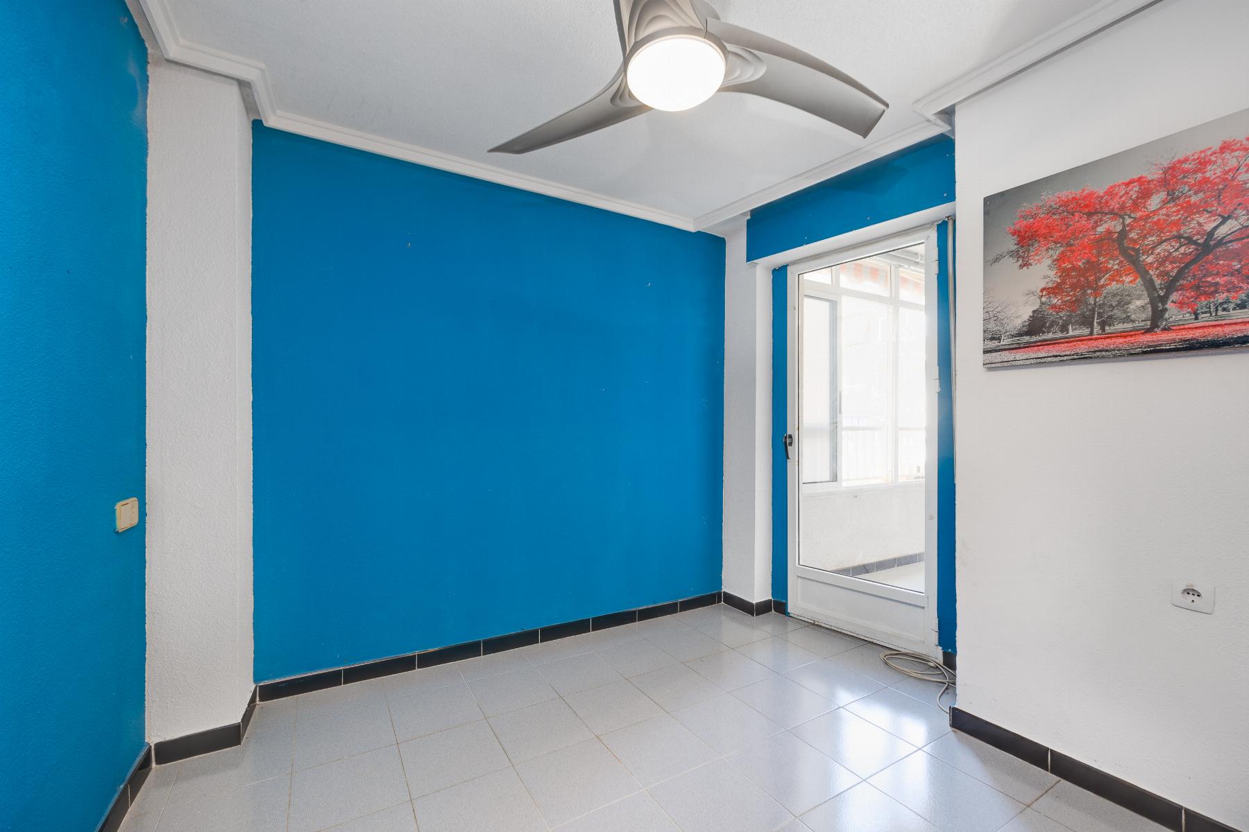 Blue-walled room with white trim, a white ceiling fan, and a glass door to the outside; a red-tree landscape painting hangs on the wall to the right.