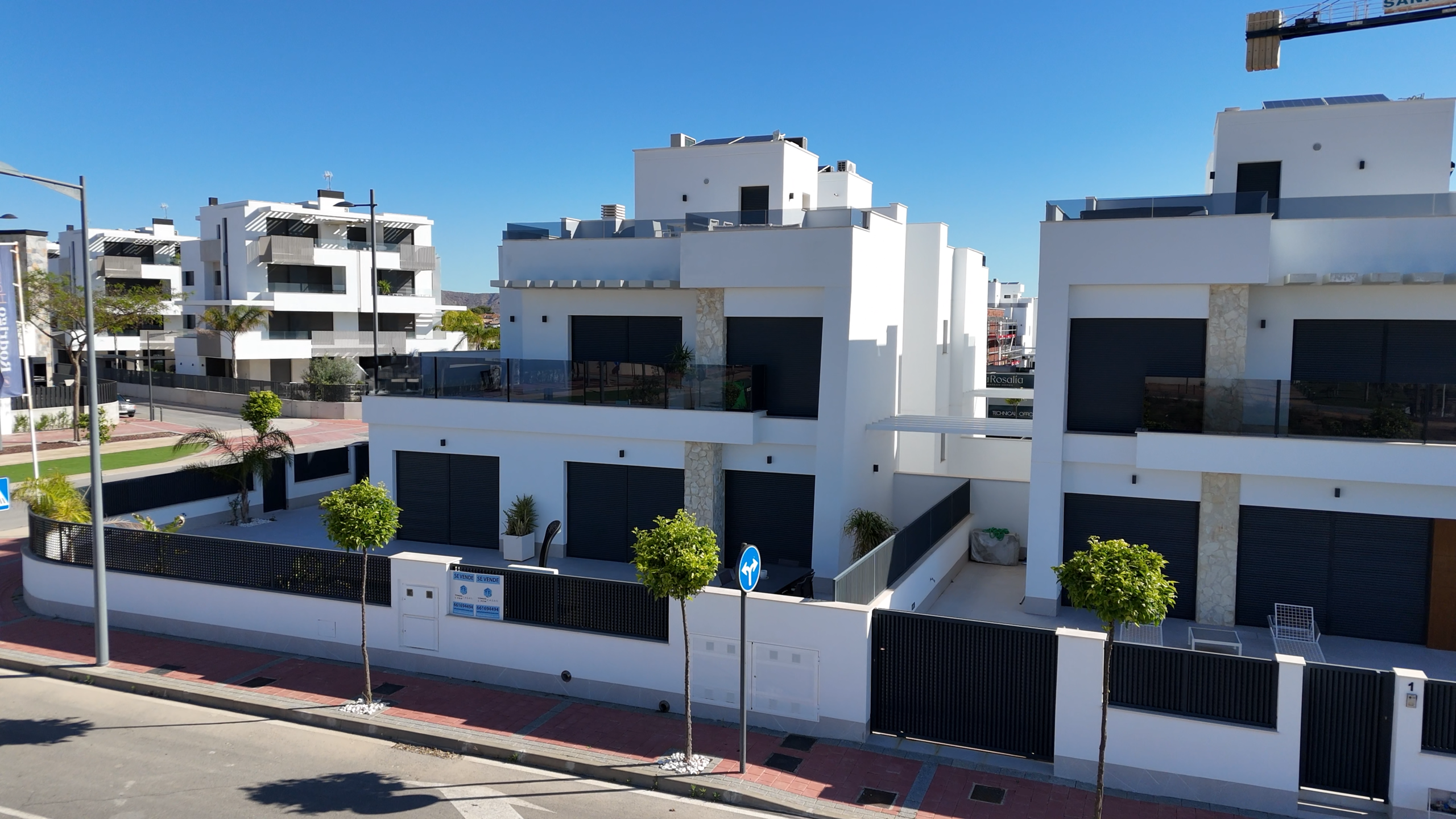 Modern white apartment buildings with black shutters and glass balconies along a sunny street.