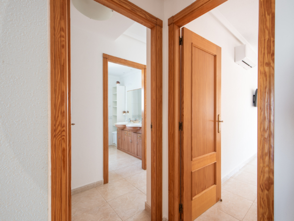 Hallway with tall wooden doors open into a bathroom featuring a double-sink vanity and tiled floor