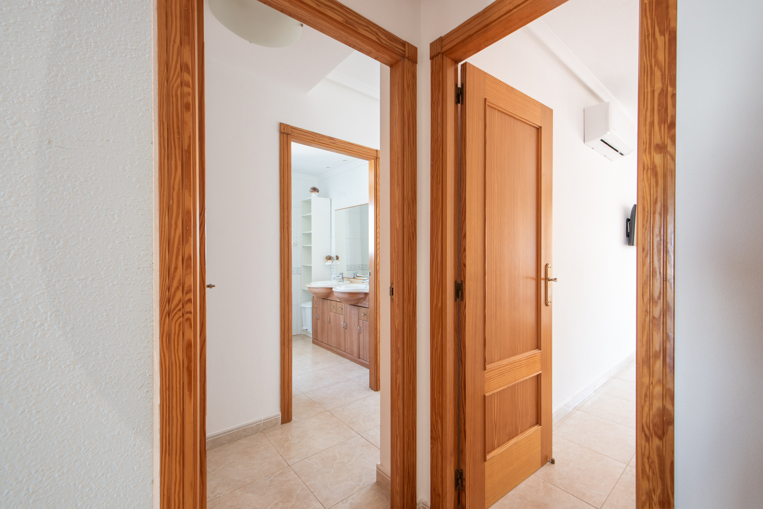 Hallway with tall wooden doors open into a bathroom featuring a double-sink vanity and tiled floor