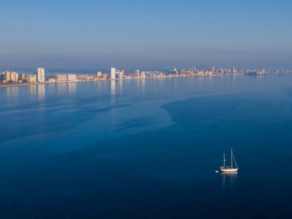 Uitzicht over het water op de kustlijn van La Manga met een zeilboot, in de omgeving van nieuwbouw in La Manga Club