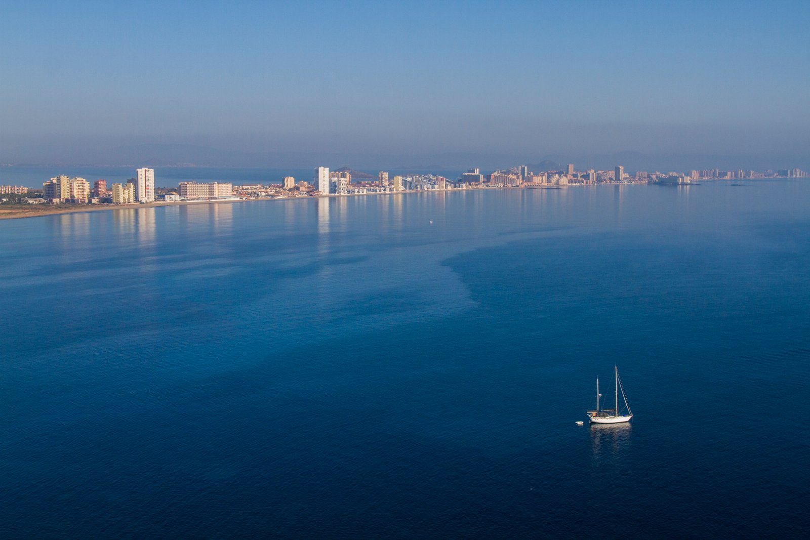 Uitzicht over het water op de kustlijn van La Manga met een zeilboot, in de omgeving van nieuwbouw in La Manga Club