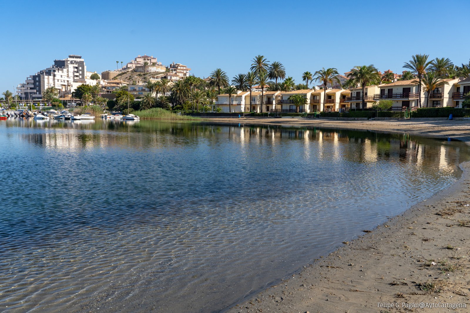 Zandstrand met rustig water, palmbomen en bebouwing aan de kust, in de omgeving van nieuwbouw in La Manga Club