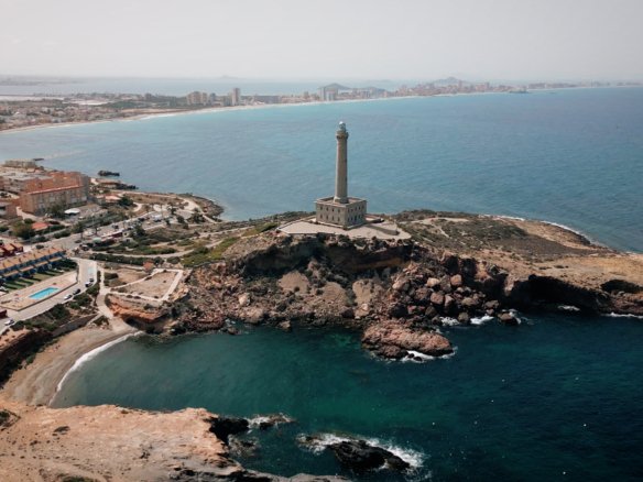 Luchtfoto van de vuurtoren van Cabo de Palos met rotsbaaien en zee, in de omgeving van nieuwbouw in La Manga Club