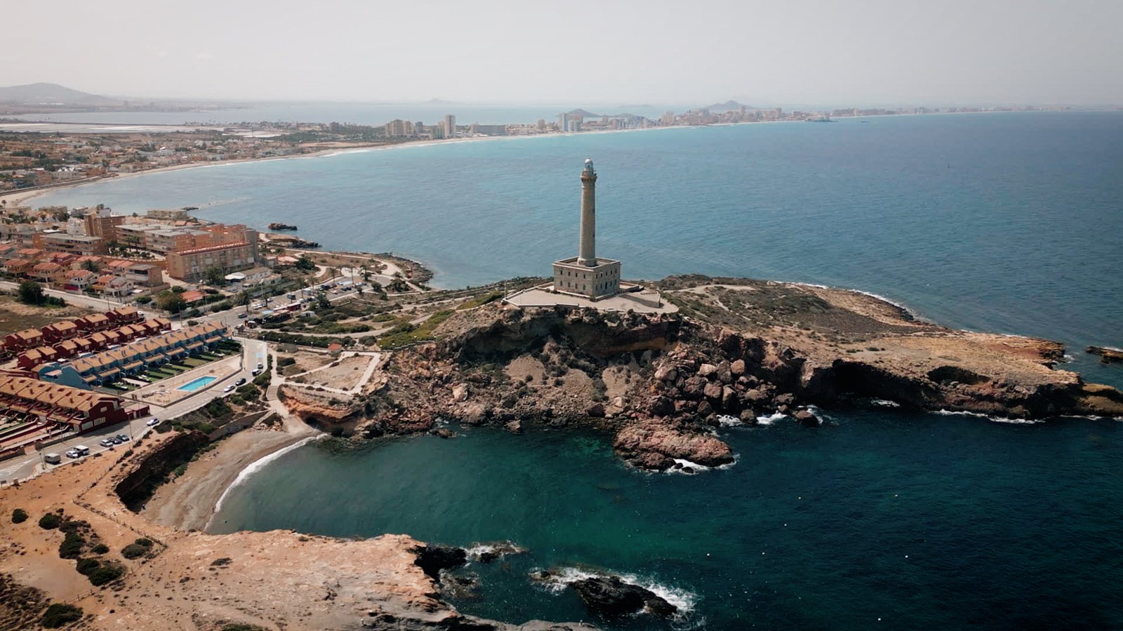 Luchtfoto van de vuurtoren van Cabo de Palos met rotsbaaien en zee, in de omgeving van nieuwbouw in La Manga Club