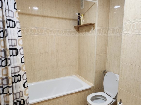 Ligbad met douchegordijn en sanitair in de badkamer van het appartement.