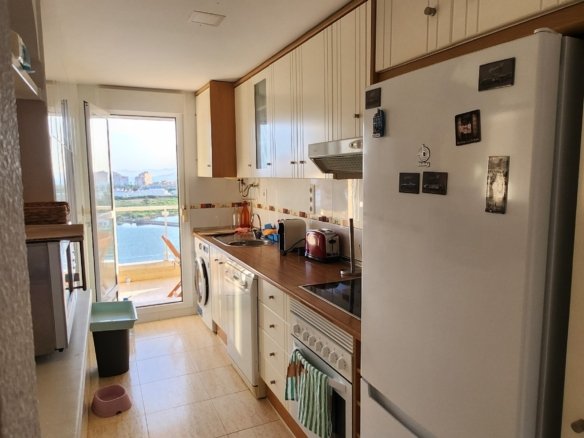 Keuken met koelkast en doorkijk naar de lichte woonkamer en het terras.