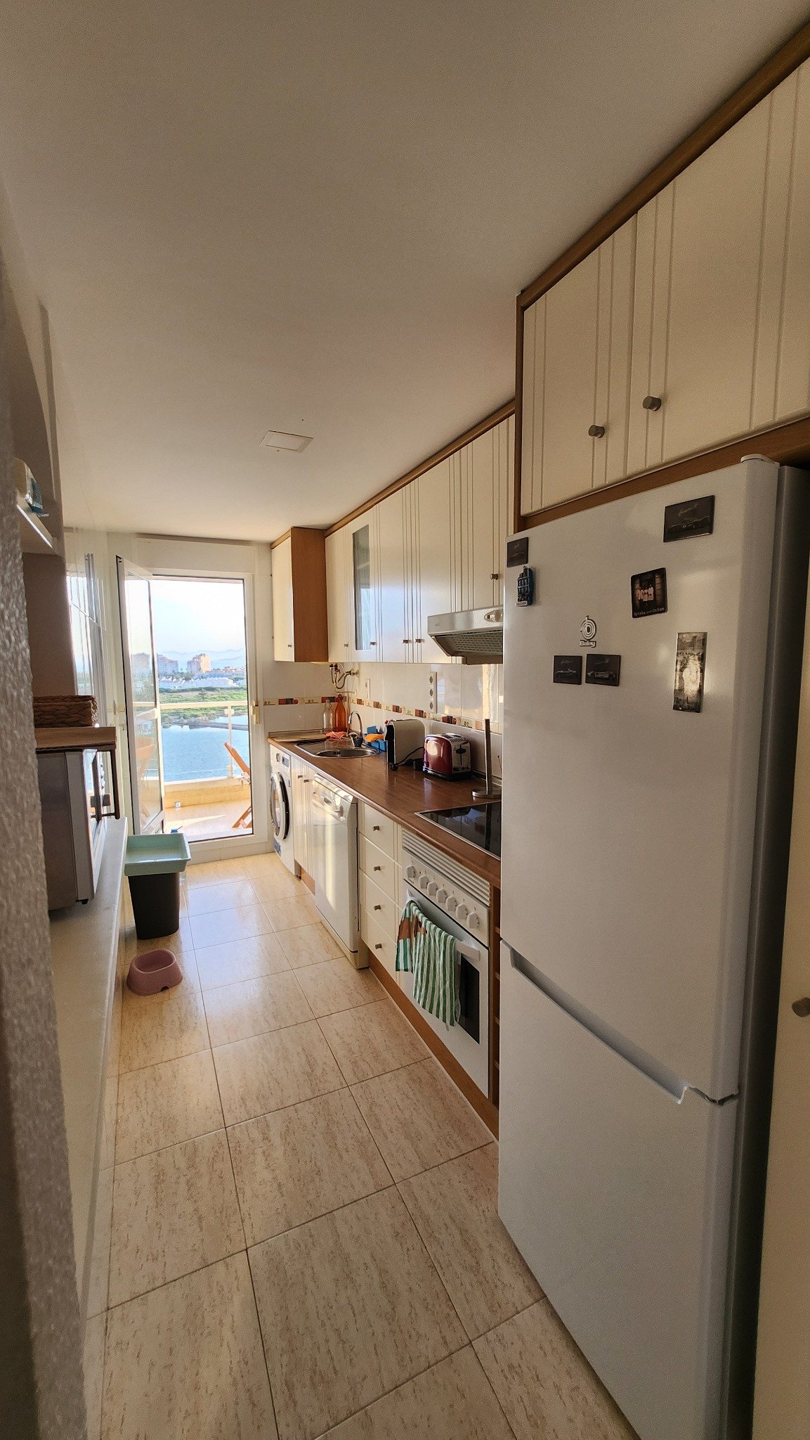 Keuken met koelkast en doorkijk naar de lichte woonkamer en het terras.