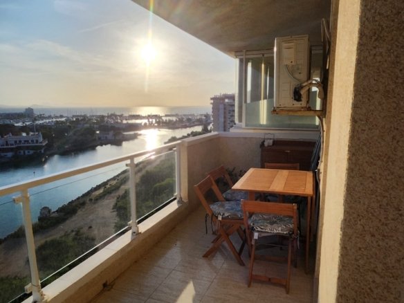 Overdekt terras met zitplaatsen en glazen balustrade bij het appartement.