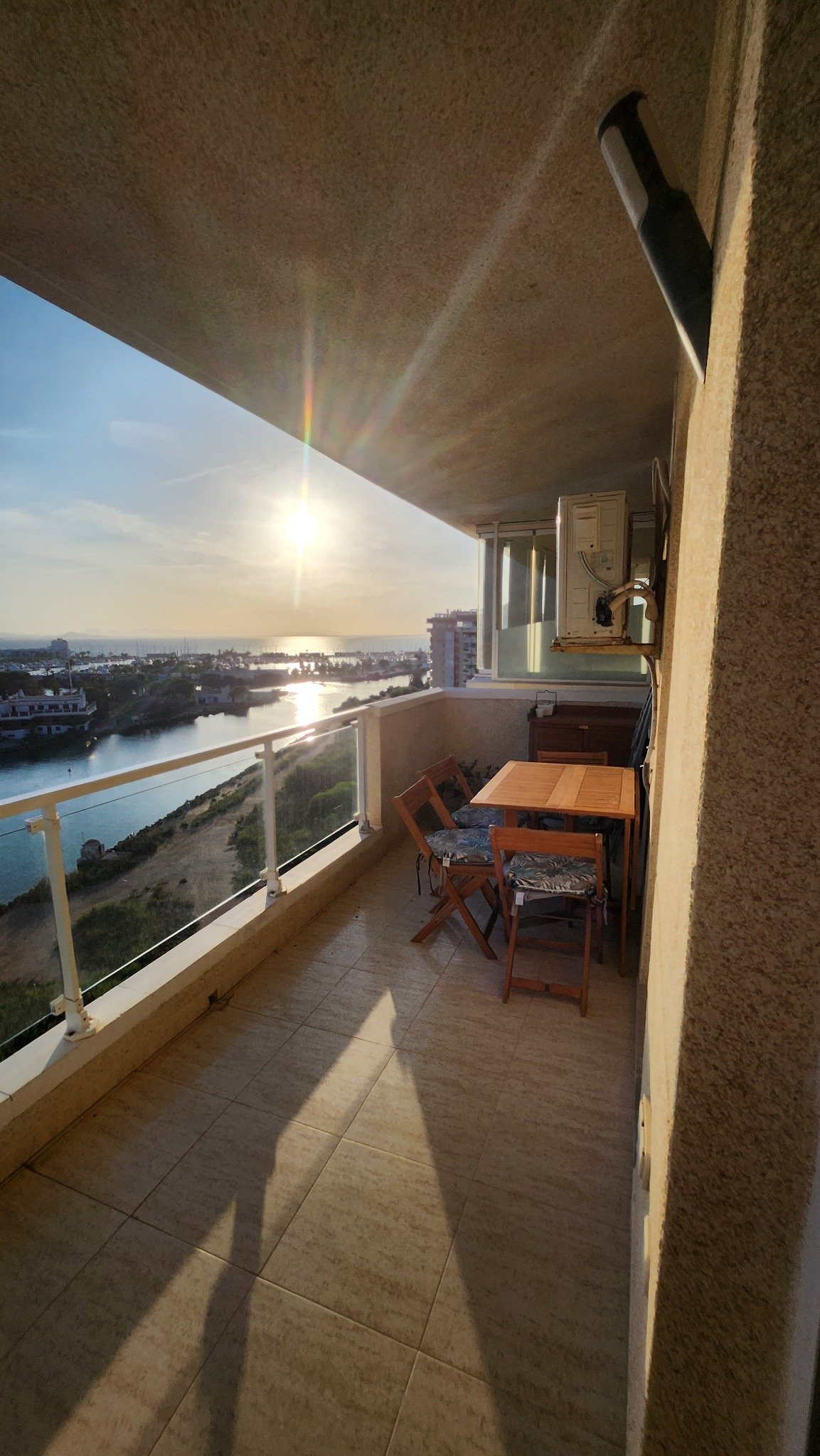 Overdekt terras met zitplaatsen en glazen balustrade bij het appartement.