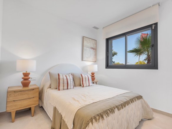 Een slaapkamer met een bed, nachtkastje en raam met uitzicht op een palmboom.