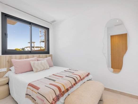 Slaapkamer met bed, kussens en een grote spiegel aan de muur.