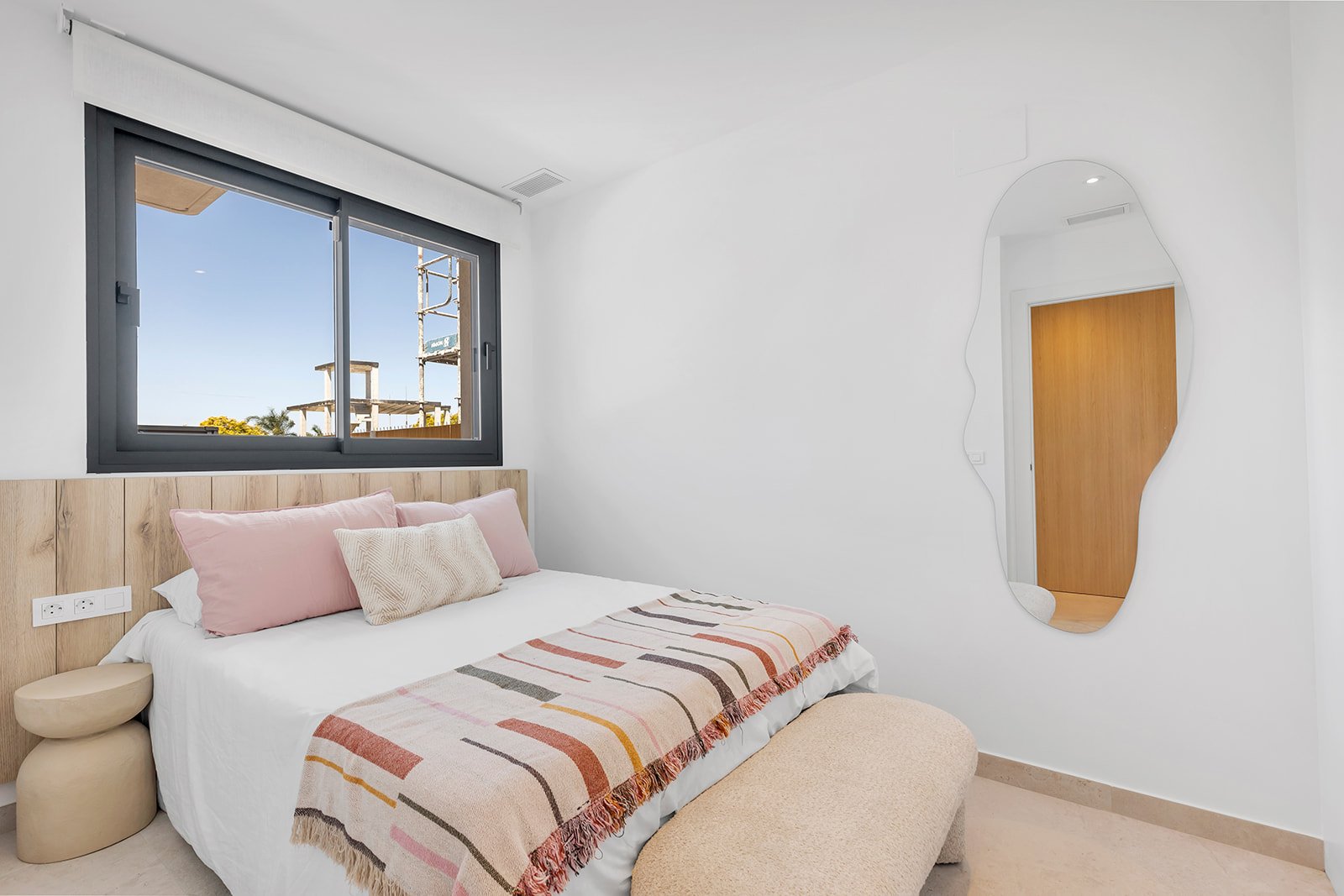Slaapkamer met bed, kussens en een grote spiegel aan de muur.