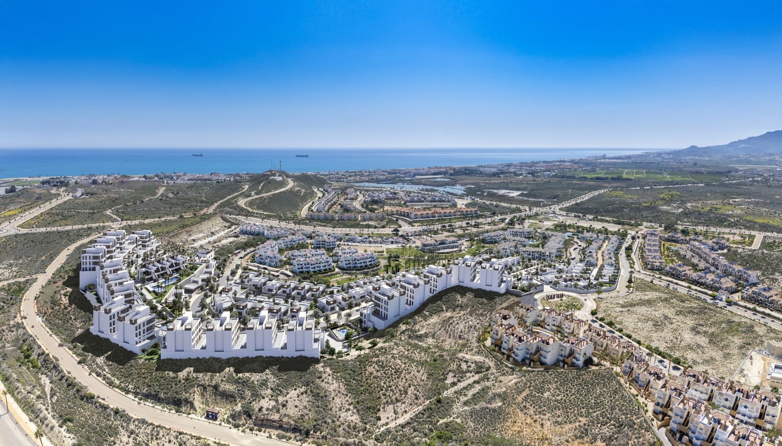 Luchtbeeld van een woonwijk met witte gebouwen en woningen in een droog landschap aan zee.
