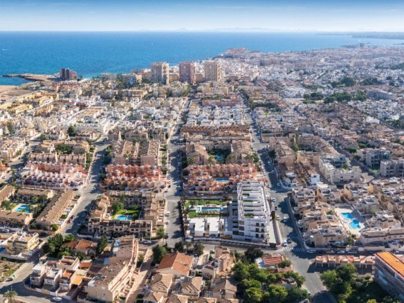 Luchtfoto van een stedelijk gebied met woningen en de zee op de achtergrond.