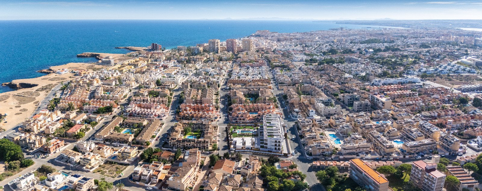Luchtfoto van een stedelijk gebied met woningen en de zee op de achtergrond.