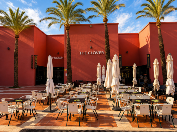 Een restaurant met de naam 'The Clover' en een openluchtterras met witte tafels en stoelen, omringd door palmbomen.